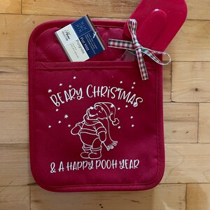 May include: Red quilted pot holder with a white outline of Winnie the Pooh wearing a Santa hat and the text "Beary Christmas & A Happy Pooh Year".