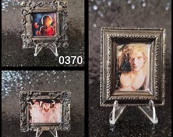 May include: Three ornate gold picture frames with glass fronts and black stands. The frames contain images of a character from a horror movie, a group of people, and a person with long hair.