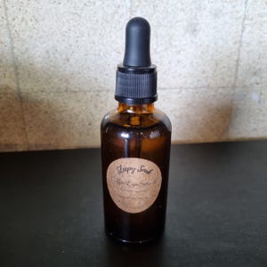 May include: A brown glass bottle with a black dropper top. The bottle is labeled "Sleepy Soak Coffee Eye Serum".