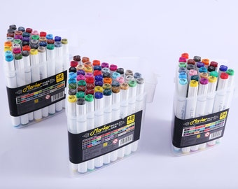 Könnte beinhalten: Drei Sets farbiger Marker auf Alkoholbasis in transparenten Kunststoffgehäusen. Die Marker haben weiße Schäfte und farbige Kappen, wobei die Anzahl der Marker in jedem Set auf der Verpackung angegeben ist. Der Text "Marker" ist sichtbar.