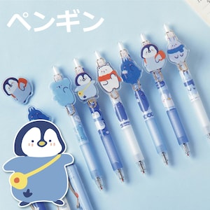 May include: A selection of blue and white pens featuring animal-themed toppers, such as penguins and koalas. The pens have a light blue barrel and are displayed on a light blue surface. The Japanese word for "penguin" is visible.