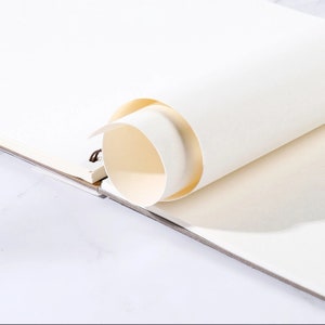 K&ouml;nnte beinhalten: Ein Skizzenbuch mit cremefarbenen Seiten, teilweise aufgerollt. Die Spiralbindung ist auf der linken Seite sichtbar. Das Papier hat eine glatte Textur, und die Kanten sind leicht gebogen, was auf Neuheit hindeutet.