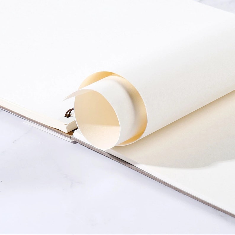 K&ouml;nnte beinhalten: Ein Skizzenbuch mit cremefarbenen Seiten, teilweise aufgerollt. Die Spiralbindung ist auf der linken Seite sichtbar. Das Papier hat eine glatte Textur, und die Kanten sind leicht gebogen, was auf Neuheit hindeutet.