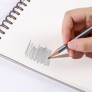K&ouml;nnte beinhalten: Eine Hand, die einen grauen Bleistift h&auml;lt und auf einem wei&szlig;en Spiralnotizblock skizziert. Der Bleistift erzeugt eine Reihe grauer Linien auf dem Papier, was die Verwendung des Bleistifts zum Zeichnen oder Schreiben demonstriert. Die Spiralbindung des Notizblocks ist sichtbar.