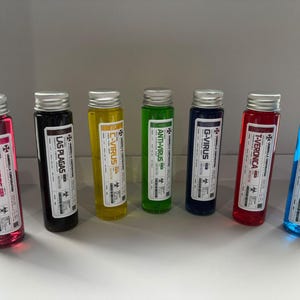 Op de afbeelding: Zeven cilindrische flessen van helder glas met zilveren schroefdoppen, elk gevuld met een vloeistof in een andere kleur: roze, zwart, geel, groen, donkerblauw, rood en lichtblauw. Elke fles heeft een wit etiket met tekst en een biohazard-symbool.