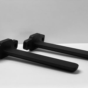 May include: Two black plastic brackets with a curved shape and a long, straight arm. The brackets are designed to be mounted to a wall or other surface.