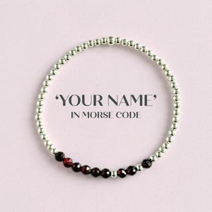 Könnte beinhalten: Ein Armband mit silberfarbenen Perlen und einem Abschnitt aus dunkelroten Perlen. Das Armband ist kreisförmig und vor einem hellrosa Hintergrund angeordnet. Der Text auf dem Bild lautet 'YOUR NAME' IN MORSE CODE.