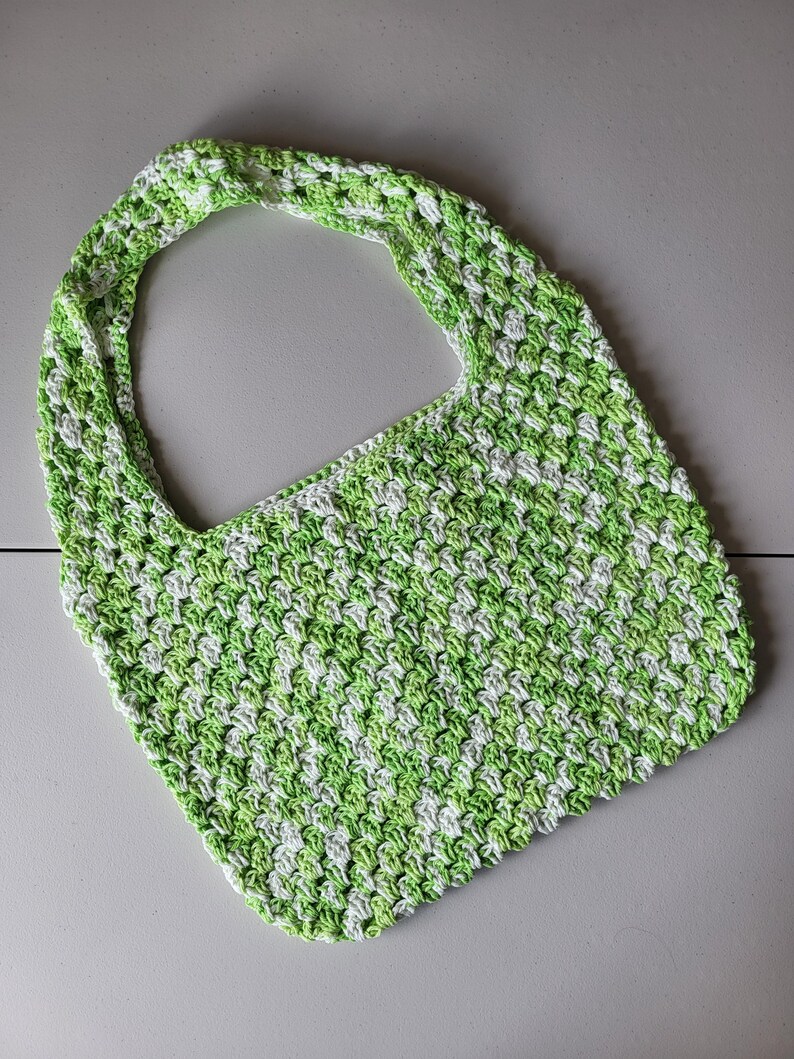 Pu&ograve; includere: Una borsa tote all'uncinetto con un motivo verde e bianco. La borsa presenta un manico largo e integrato e un design a punto strutturato. La borsa &egrave; realizzata in filato morbido ed &egrave; adatta per trasportare vari oggetti.
