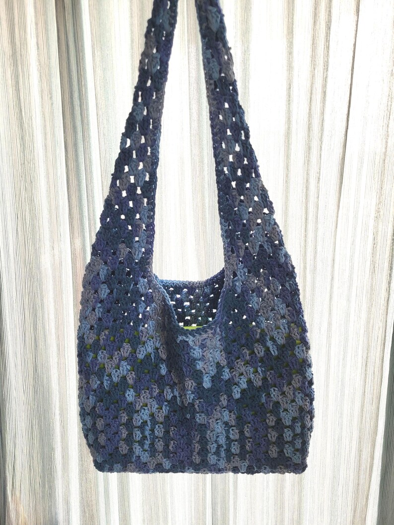 Pu&ograve; includere: Una borsa tote all'uncinetto blu con un motivo a granny square. La borsa presenta lunghe cinghie e un interno spazioso. Il design a trama aperta aggiunge un tocco di consistenza. Un accessorio elegante e pratico.