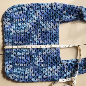 Pu&ograve; includere: Borsa a tracolla all'uncinetto fatta a mano nei toni del blu. La borsa &egrave; larga circa 35,5 cm. Il motivo all'uncinetto crea un aspetto strutturato. Anche la tracolla &egrave; all'uncinetto e attaccata alla borsa. La borsa &egrave; su una superficie chiara.