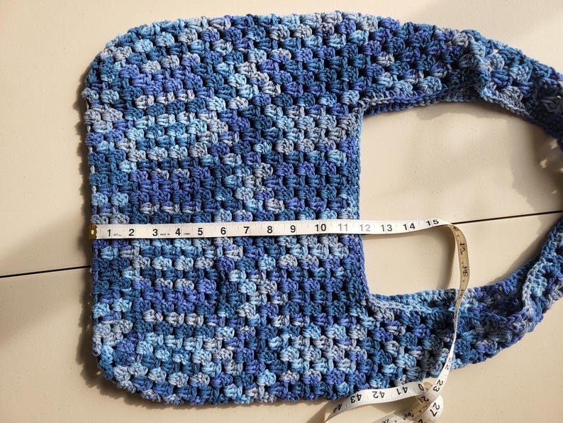 Pu&ograve; includere: Borsa a tracolla all'uncinetto fatta a mano nei toni del blu. La borsa &egrave; larga circa 35,5 cm. Il motivo all'uncinetto crea un aspetto strutturato. Anche la tracolla &egrave; all'uncinetto e attaccata alla borsa. La borsa &egrave; su una superficie chiara.