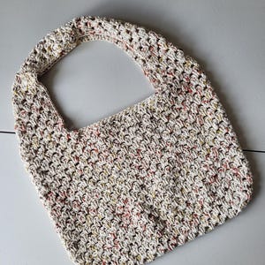 Pu&ograve; includere: Una borsa tote all'uncinetto fatta a mano, in una palette di colori neutri. La borsa presenta un motivo a punto strutturato con macchie rosse, gialle e marroni. Il cinturino &egrave; integrato nel design della borsa, creando un aspetto senza cuciture. Questa borsa versatile &egrave; perfetta per l'uso quotidiano.