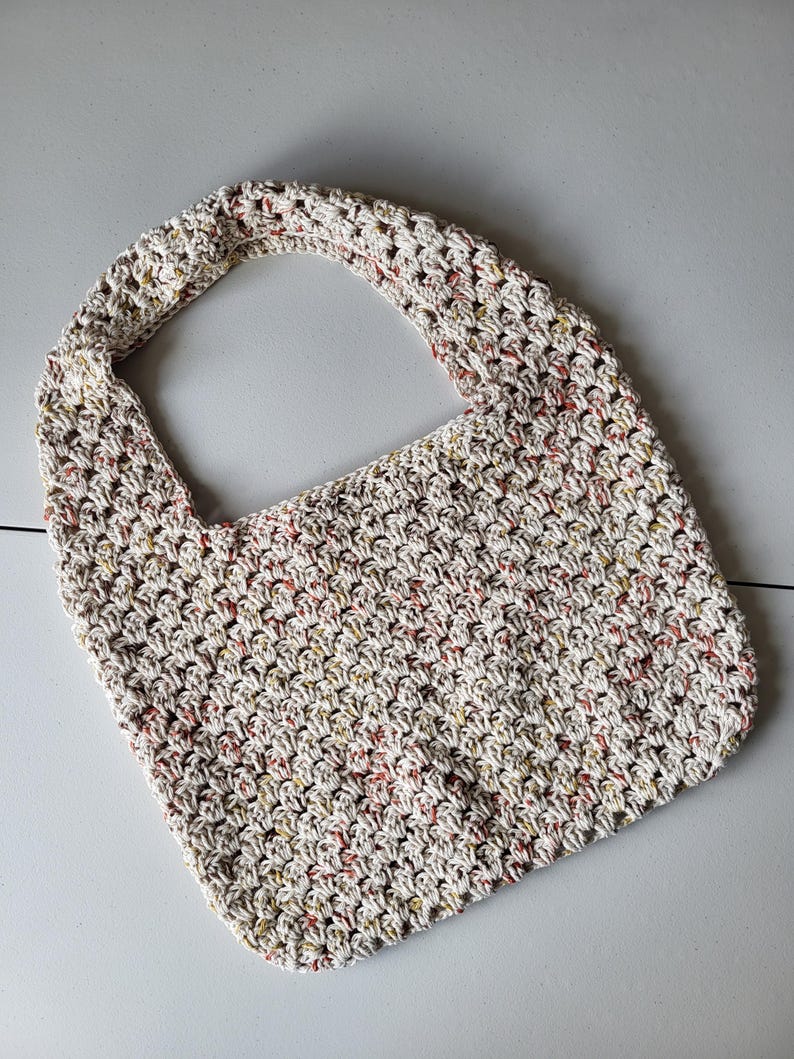 Pu&ograve; includere: Una borsa tote all'uncinetto fatta a mano, in una palette di colori neutri. La borsa presenta un motivo a punto strutturato con macchie rosse, gialle e marroni. Il cinturino &egrave; integrato nel design della borsa, creando un aspetto senza cuciture. Questa borsa versatile &egrave; perfetta per l'uso quotidiano.