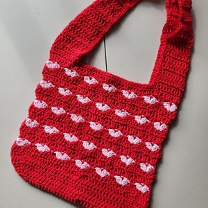 Pu&ograve; includere: Borsa a tracolla rossa all'uncinetto con un motivo a cuori bianchi. La borsa ha una lunga tracolla ed &egrave; realizzata in filato strutturato. La borsa fatta a mano ha uno stile casual e femminile.