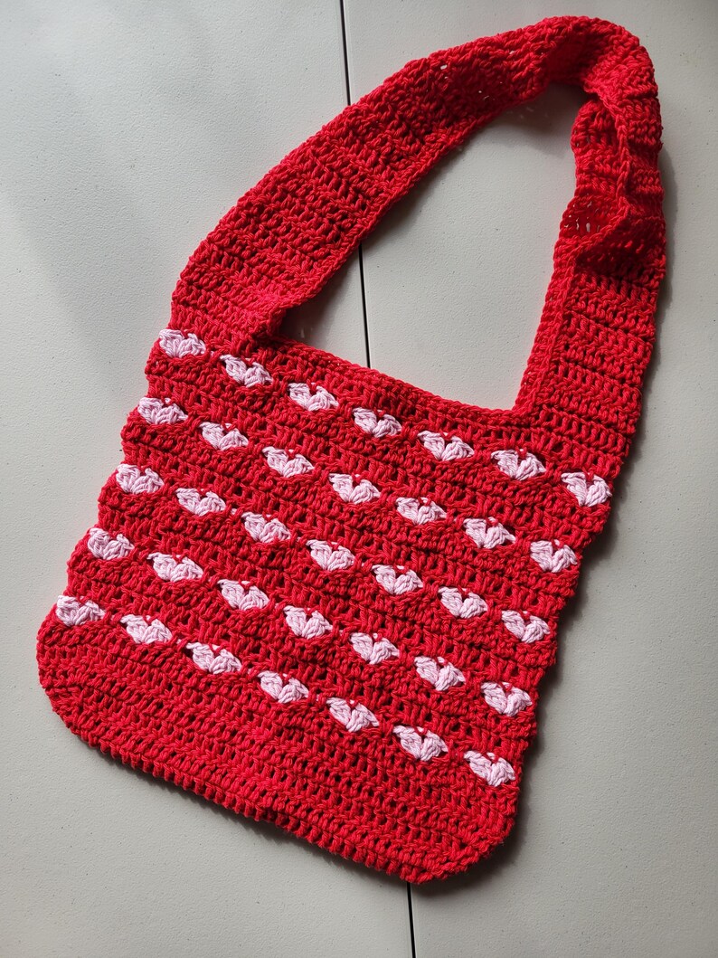 Pu&ograve; includere: Borsa a tracolla rossa all'uncinetto con un motivo a cuori bianchi. La borsa ha una lunga tracolla ed &egrave; realizzata in filato strutturato. La borsa fatta a mano ha uno stile casual e femminile.