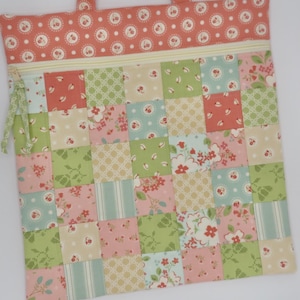 May include: A patchwork tote bag with a variety of floral and geometric patterns in shades of pink, green, and blue. The top section features a dotted pattern and a zipper closure. The bag has two small handles.