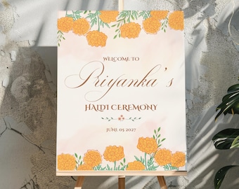 May include: A welcome sign for a Haldi ceremony, featuring a floral design with orange marigolds and green leaves. The sign reads "Welcome to Priyanka's Haldi Ceremony, June 05 2027".