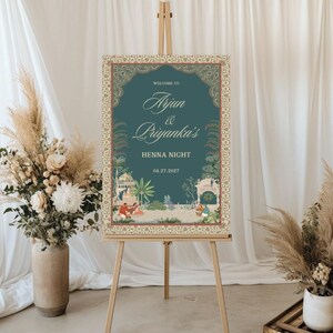 May include: A teal blue welcome sign with a gold ornate border and a floral design. The sign reads "Welcome to Arjun & Priyanka's Henna Night 04.27.2022".