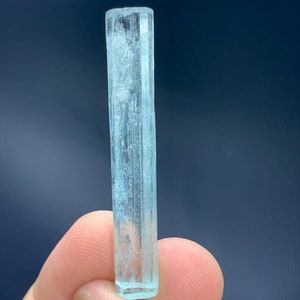 May include: A translucent, light blue aquamarine crystal with a rectangular prism shape. The crystal is about 2 inches long and has a smooth, polished surface.