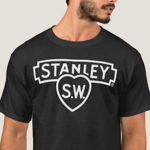 May include: Black t-shirt with a white graphic of the Stanley S.W. logo. The logo features a heart with the letters S.W. inside and the word Stanley above the heart.