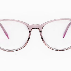 Pode incluir: Um par de óculos redondos de cor rosa com lentes transparentes.