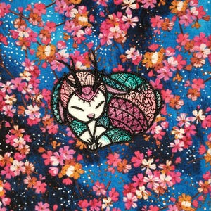 May include: Embroidered patch featuring a stylized, sleeping creature with antlers, in shades of white, teal, and pink. The patch is set against a blue background with a floral pattern of pink and orange blossoms.