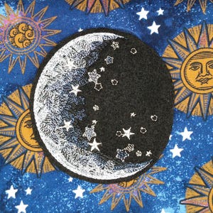 May include: A black and white embroidered crescent moon patch with stars, set against a blue celestial background with sun and star patterns. The patch is a circular shape and features detailed stitching.