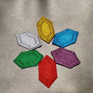 May include: Six colorful, embroidered patches shaped like gemstones. The patches are arranged in a star shape and are in the colors red, green, purple, blue, silver, and yellow.