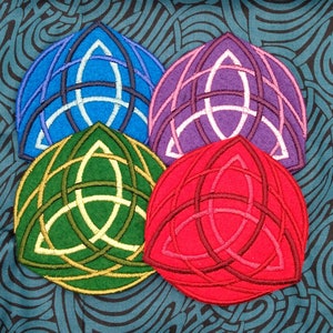 May include: Four embroidered Celtic knot triquetra patches in different colors: blue, purple, green, and red. The patches are on a blue and black patterned fabric.