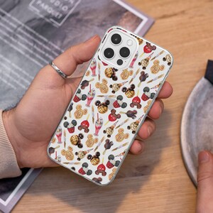 Könnte beinhalten: Eine weiße iPhone-Hülle mit einem bunten Muster aus Comic-Mickey-Mouse-Ohren, Cupcakes, Eiswaffeln und anderen Leckereien. Die Hülle hat eine transparente Rückseite und einen weißen Rand.