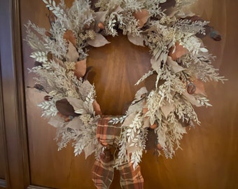 May include: A white and brown wreath with a plaid bow. The wreath is made of dried flowers and branches.