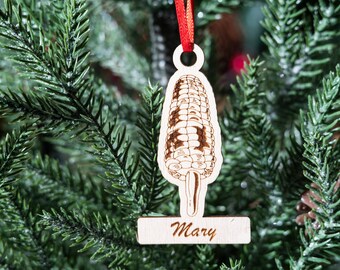 Puede incluir: Adorno de Navidad de madera con forma de mazorca de maíz con el nombre "Mary" escrito en una etiqueta debajo.
