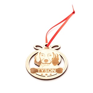 May include: Wooden Christmas ornament shaped like a circle with a dog's face and the name "TYSON" engraved on it. The ornament is attached to a red ribbon.