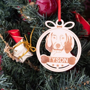 May include: A wooden Christmas ornament shaped like a dog bone with a dog's head inside. The ornament is painted white and has the name "TYSON" written on it.