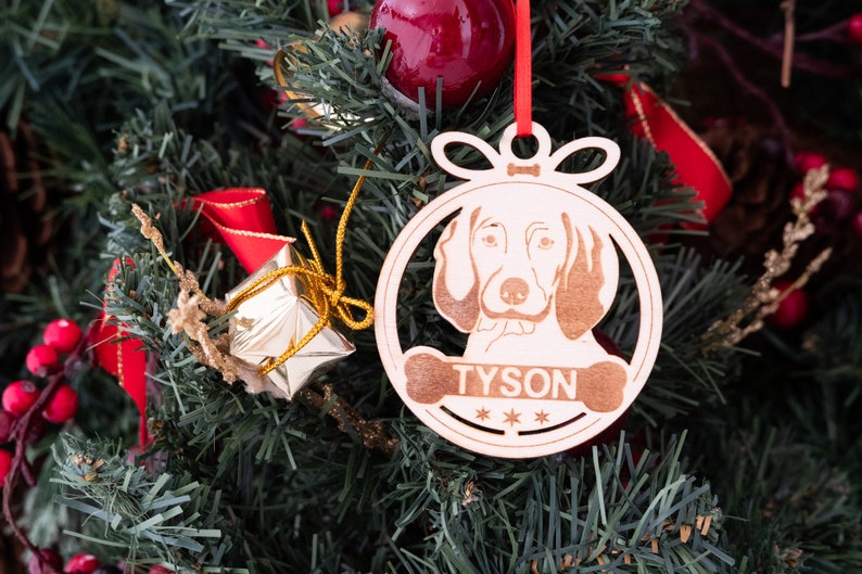 May include: A wooden Christmas ornament shaped like a dog bone with a dog's head inside. The ornament is painted white and has the name "TYSON" written on it.