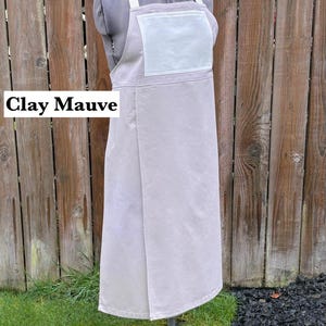 May include: A clay mauve apron with a white pocket and straps is displayed on a mannequin. The apron is made of a soft fabric and has a simple, functional design. The text "Clay Mauve" is visible in the image.