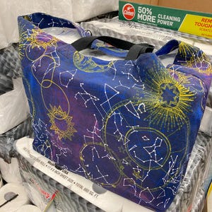 May include: A blue tote bag with a constellation pattern featuring stars, moons, and suns in yellow, white, and purple. The bag has black straps and is made in the USA. 180 sheets per roll, 11 x 6 inch sheet size, total 880 sq. ft.