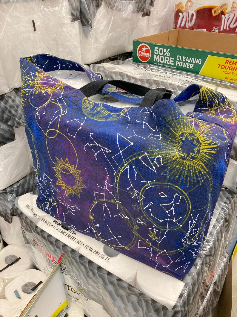 May include: A blue tote bag with a constellation pattern featuring stars, moons, and suns in yellow, white, and purple. The bag has black straps and is made in the USA. 180 sheets per roll, 11 x 6 inch sheet size, total 880 sq. ft.