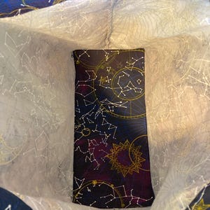 May include: A dark purple tote bag with a white lining. The exterior of the bag features a constellation pattern with gold accents. The interior of the bag is lined with a white fabric.