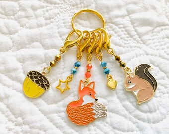 May include: A gold charm keychain featuring a fox, squirrel, acorn, star, and heart charms. The charms are attached to a gold ring with multiple loops. The charms are decorated with blue, red, and gold beads.