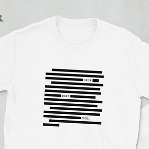 Può includere: T-shirt bianca con un design grafico nero. Il design presenta linee nere orizzontali con le parole "GROW", "MORE" e "FOOD" intercalate. La maglietta è realizzata in un materiale morbido ed è adatta per l'abbigliamento casual.