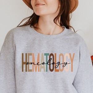 May include: A gray sweatshirt with the text "HEMATOLOGY oncology" in colorful letters. The letters are in shades of brown, orange, and green.