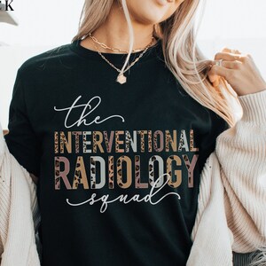 May include: Black t-shirt with the text "The Interventional Radiology Squad" in a leopard print design.