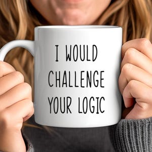 May include: White ceramic mug with the text "I WOULD CHALLENGE YOUR LOGIC" in black, held by a person. The mug has a curved handle and a glossy finish. The background is blurred, focusing on the mug's message.