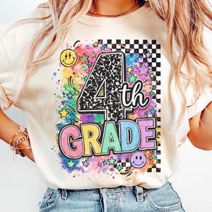 May include: An ivory t-shirt featuring a graphic print with the text 4th GRADE. The design includes a black and white leopard print number 4, colorful block letters, a black and white checkerboard pattern, stars, and smiley faces on a watercolor background.
