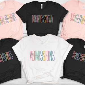 May include: Six t-shirts with different job titles printed on them in rainbow colors. The titles are "Medical Records", "Executive Secretary", "Scheduler", "Human Resources", "Admissions", and "Transportation".