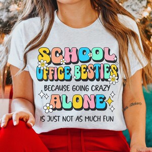 May include: White t-shirt with a colorful graphic that says "School Office Besties because going crazy alone is just not as much fun".