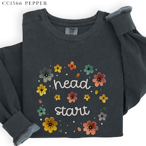 May include: A dark gray sweatshirt with a floral design and the text "head start" in white.