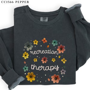 May include: A dark gray sweatshirt with a floral design and the text "recreation therapy" in white.
