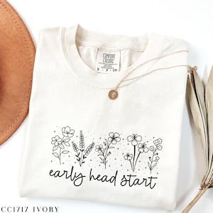 May include: A cream-colored t-shirt with a black floral design and the text "early head start".